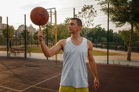 男子篮球运动员在户外场上用手指旋转球男子运动员在街头足球训练夏季体育场上穿运动服图片