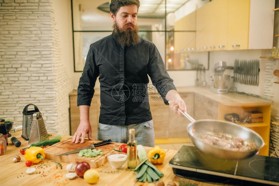 男人在餐桌上用电炉煮猪肉男人在锅里用蔬菜煮肉图片
