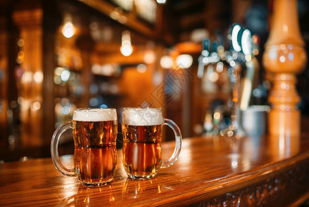 木制酒吧柜台上的两杯啤酒宏观没有人octfes符号或概念杯子上装有金饮料和泡沫在酒吧的桌子上闭路背景模糊图片
