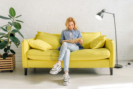 年轻女子在黄色沙发上看书高清图片