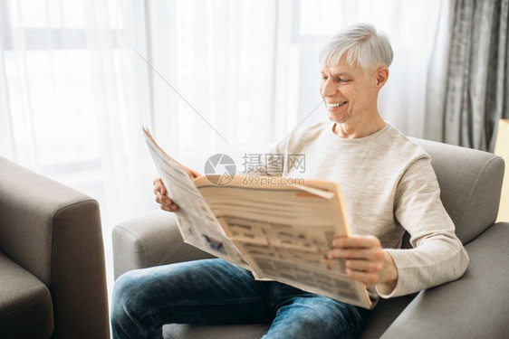 成年男子坐在沙发上和家里看报纸成年男子用扶手椅放松成年男子坐在沙发上和看报纸图片