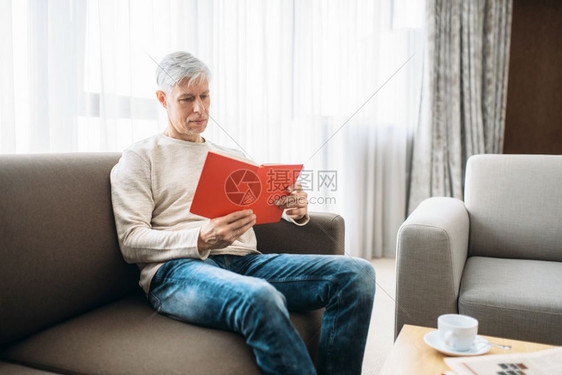穿牛仔裤的成年男子用扶手椅放松男子在家里用笔记本坐在沙发上图片