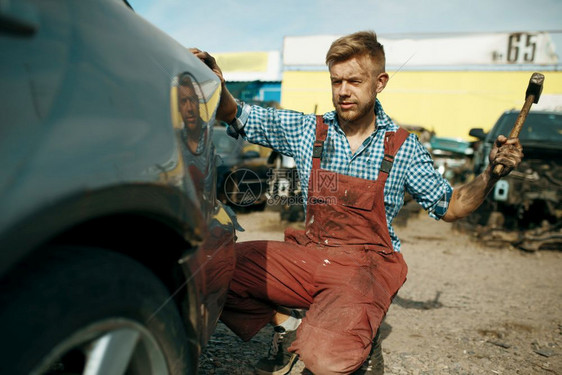 男修理工在汽车垃圾场上用锤子砸车图片