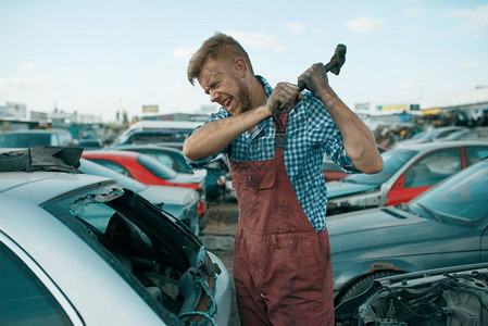 男修理工在汽车垃圾场上用锤子砸车图片