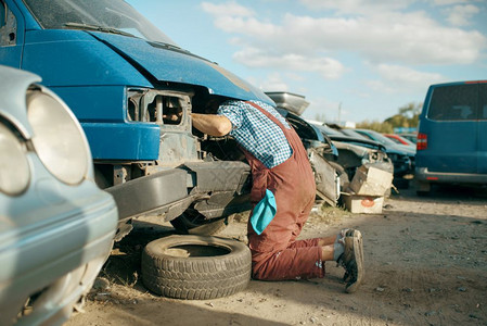 男机械师在汽车垃圾场将头盖在车下修理汽车图片