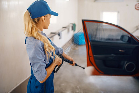 身穿制服的妇女用高压水枪清洁车辆车门背景图片