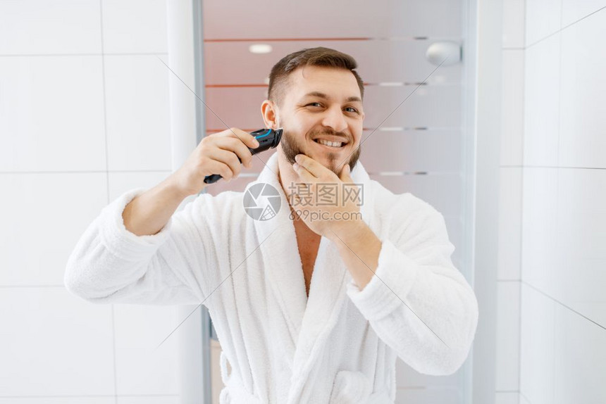 穿浴袍的男子在浴室用电动剃刀刮胡子图片