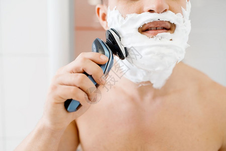 男子一脸泡沫在浴室用电动剃须刀剃须图片