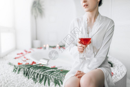 穿着白色浴袍的优雅女子坐在浴衣的边缘上面装饰着玫瑰花瓣豪华的浴室内坐在衣上装饰着玫瑰花瓣的女人图片