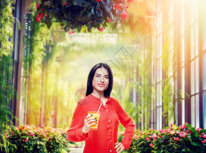 穿着衬衫和草帽的快乐女人喝着新鲜的橙汁公园背景喝着黄色维生素饮料健康活方式的年轻女孩喝着橙汁图片