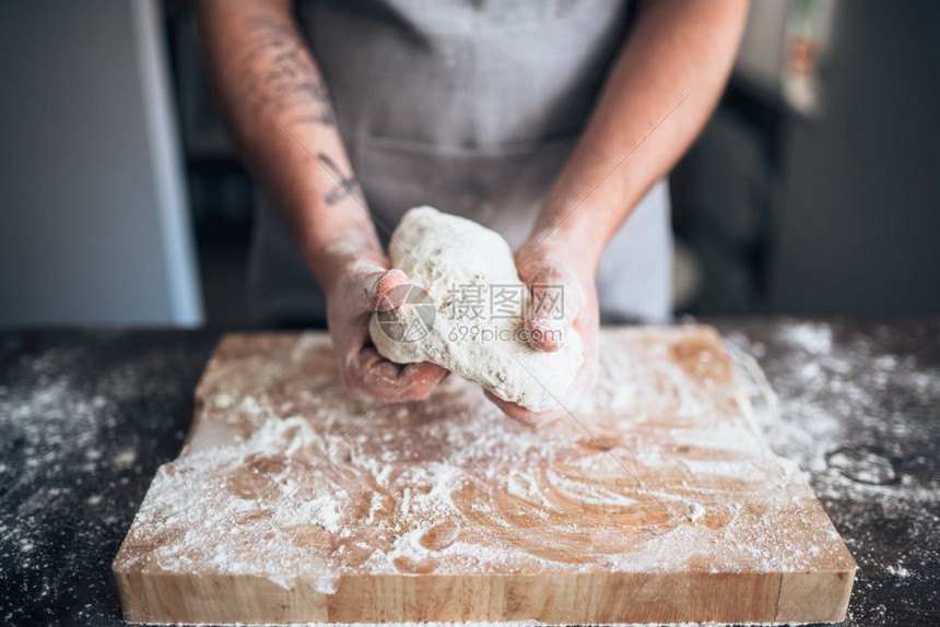 男面包师亲手在木桌上揉捏面团图片
