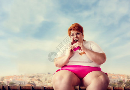 体重超的女人坐在屋顶上吃甜蛋糕懒惰肥胖贪食不健康的物吃胖女人图片