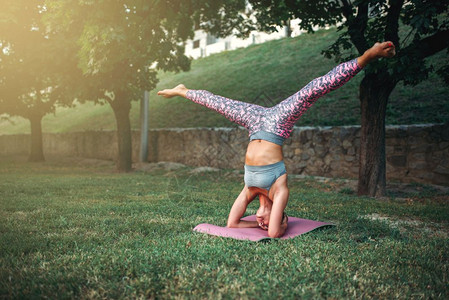女青年在公园里使用瑜伽垫进行户外运动倒立图片