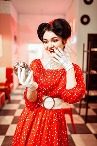 令人惊讶的针头女孩看着闹钟古老的内地咖啡馆背景流行的美国时尚50和6年代红礼服配有波尔卡点明亮的化妆品图片