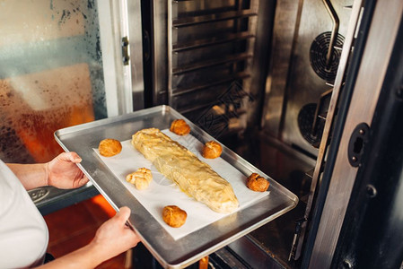 男厨师双手在烤炉的金属烘板上加苹果螺旋甜面包点准备图片