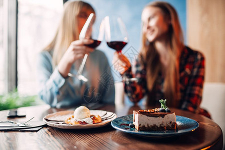 女孩们喝红酒在餐厅吃甜点桌上有巧克力蛋糕和酒图片