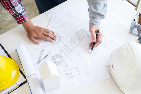 个人和工程师手绘计划与建筑师设备在桌子上讨论的建筑师团队工作和流量建设概念图片