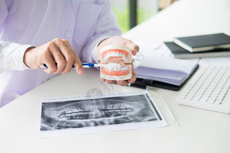 在牙科办公室专业诊所集中的牙医坐在桌子上抽取下巴的牙齿模型样本图片