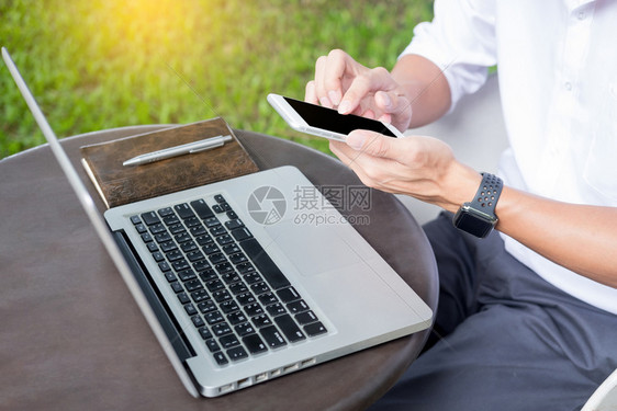 在自然硬木桌外工作的人在现代笔记本电脑上工作的人坐在自然硬木桌外绿色植物背景的阳光日户外你来自笔记本电脑概念的任何地方图片