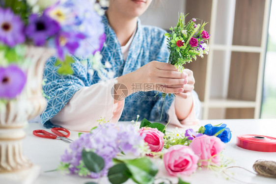 年轻女商人花卉店主在其商手工艺品和中制作或安排人工鲜花背心图片