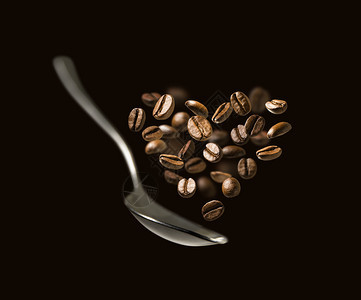 黑色背景中的勺子和心形咖啡豆图片