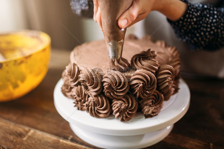 烹饪女人用注射器装饰巧克力蛋糕厨房背景自制甜品装饰妇女用烹饪注射器装饰蛋糕图片