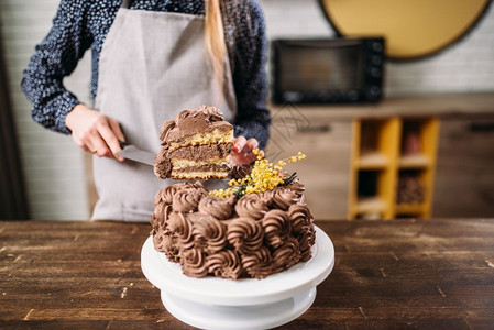 做饭的女人拿着一块巧克力蛋糕在刀片上烹饪杰作厨房在背景上自制甜点女人拿着一块巧克力蛋糕在刀片上图片