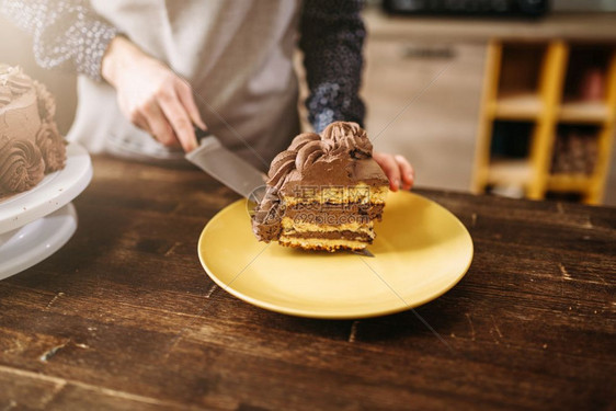 女手握着一块巧克力蛋糕在刀片上烹饪杰作厨房在背景上自制甜点图片