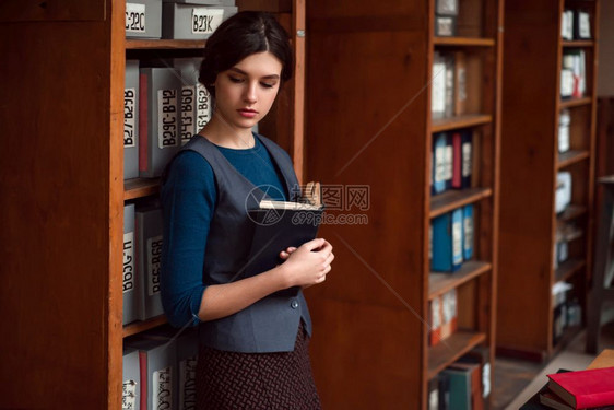 在学校图书馆架之间站立的年轻女孩图片