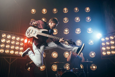 吉他手在巴斯上表演跳快照背景有灯光的舞台摇滚乐队音会吉他手在巴斯上演奏图片