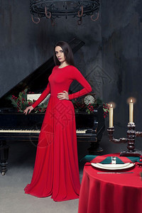 穿着红色礼服的优雅女人站在古老的钢琴前站在餐厅里面有丰富的古董图片