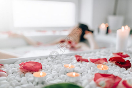 女人躺在浴池里身上沾着泡沫玫瑰花瓣烧蜡烛完全放松浴室里浪漫图片