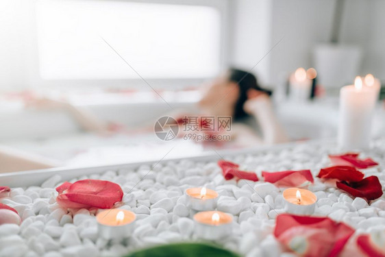 女人躺在浴池里身上沾着泡沫玫瑰花瓣烧蜡烛完全放松浴室里浪漫图片