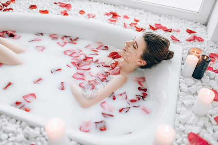 女青年睡在浴池中用泡沫玫瑰花瓣和烧蜡烛装饰完全放松在浴室里浪漫的设置女青年睡在浴池中用泡沫玫瑰花瓣图片
