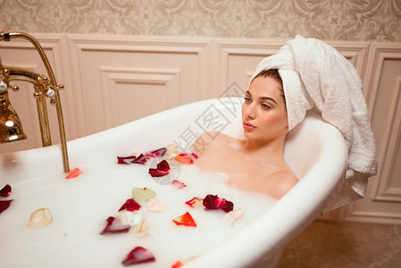 美丽的女人在充满玫瑰和花瓣的浴缸沐浴图片