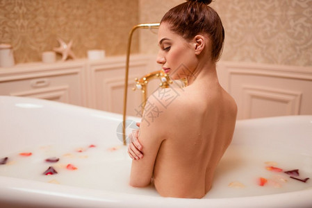 美丽的女人在带着玫瑰花瓣和泡沫浴缸里沐浴图片