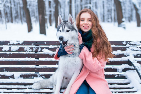 下雪的冬天年轻女子带着狗狗一起坐在公园的长凳上图片