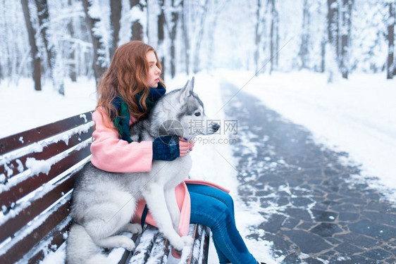 下雪的冬天年轻女子带着狗狗一起坐在公园的长凳上图片