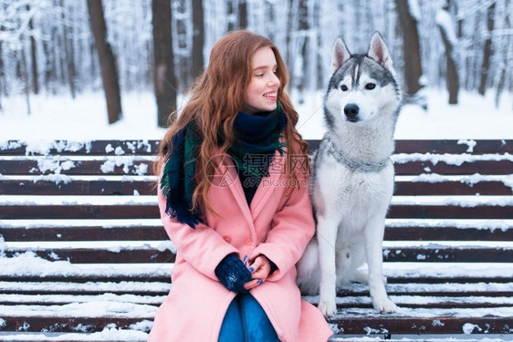 冬天美丽的女人抱着可爱的狗在外面的长凳上图片