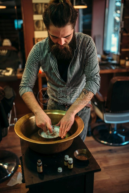 在理发店一个铜碗里准备剃须泡沫的理发师图片