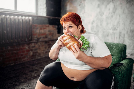 超重的女人坐在椅子上吃三明治食图片