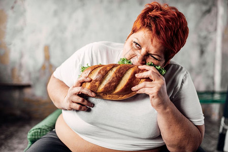 超重的女人坐在椅子上吃三明治食背景图片