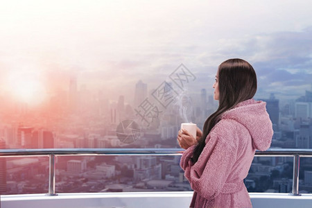 妇女在阳台上手里拿着热杯享受城市风景图片