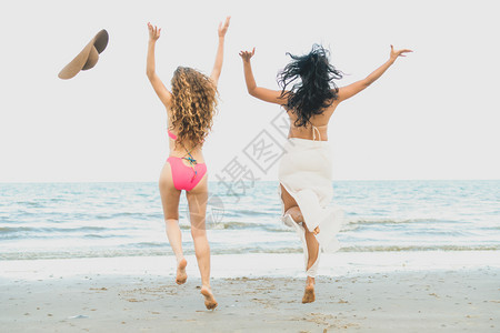 穿着比基尼的妇女在沙滩上跳跃图片