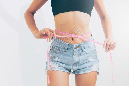 瘦弱的年轻女在吃完饭后用带子测量腰部瘦弱的女用带子测量腰部图片