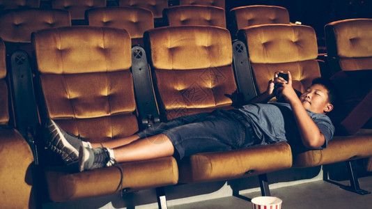 一个男孩躺下玩游戏在电影院拍照图片