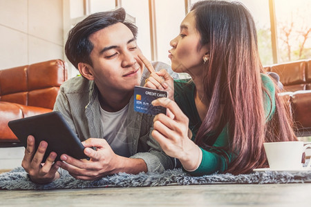 年轻夫妇使用信卡在家中的互联网站上在线购物概念图片