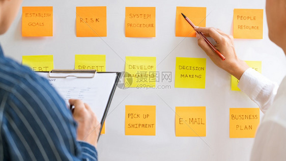 张贴粘笔记纸的年轻商业工人提醒同事在现代工作空间搭接同事时的创造集思广益图片