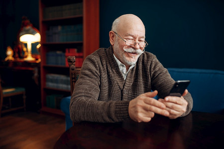 在家中办公室使用移动电话的老年男子在客厅使用智能手机的留胡子成年人在客厅使用智能手机的老年人商图片