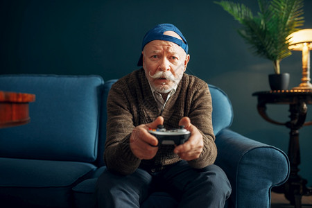 长着玩棍子的老人在沙发上玩游戏控制台图片